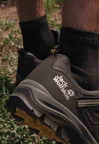 Scarpe da hiking nere con tessuto testurizzato, suola gialla e branding laterale. Il design presenta una suola robusta per trazione e supporto.