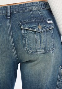 Jeans aus Denim in Mittelblau mit einer ausgewaschenen Textur. Verfügt über eine große Gesäßtasche mit Stichdetails und einem Markenetikett.