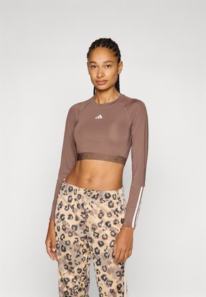 Haut court à manches longues marron avec logo ; associé à un pantalon beige à imprimé léopard avec des bandes latérales blanches. Tissu doux avec une coupe ajustée.