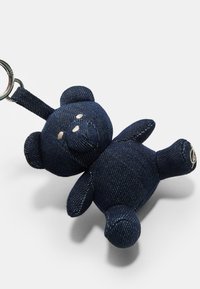 Porte-clés en denim en forme d'ours en peluche de couleur bleu foncé avec des détails brodés, des oreilles rondes et une petite boucle pour l'attache. Il présente un tissu texturé.