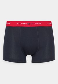 Temno modri bokserji z rdečim elastičnim pasom, ki vsebujejo bele napise "TOMMY HILFIGER", gladek material in šivane detajle.