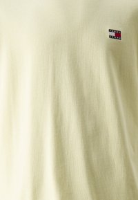 Light yellow t-shirt made of cotton, featuring a small embroidered logo in red, white, and blue on the chest. Smooth texture, regular fit.