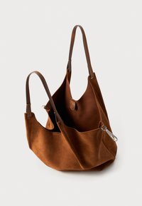Bruine suede schoudertas met twee schouderbanden,open bovenkant en een metalen sluiting. Zachte textuur, slouchy vorm en detail van een binnenzak.