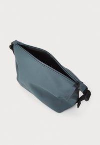 Borsa impermeabile blu con una texture liscia, chiusura a zip e tracolla nera a contrasto. Forma rettangolare con angoli arrotondati, design minimalista.