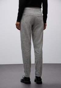 Spodnie w szaro-białą kratę houndstooth z tapered design, elastycznym pasem, bocznymi kieszeniami i teksturowanym materiałem. Noszone z czarnymi butami.