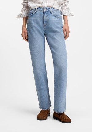 Lyseblå jeans med lige ben, båret med brune loafers og en hvid skjorte med smalle striber og opkrogede ærmer.