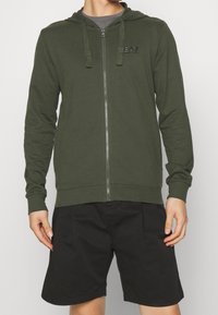 Felpa con cappuccio verde scuro con zip, cordoncini e un piccolo logo; realizzata in tessuto morbido, con maniche lunghe e vestibilità comoda.