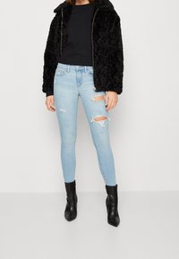 Chaqueta de piel sintética negra con cierre de cremallera, combinada con jeans ajustados rasgados de un azul claro. Botines negros de punta completan el conjunto.