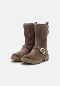 Botas de ante marrón hasta el tobillo con punta redonda, una correa lateral con un hebilla metálica cuadrada y una suela de goma texturizada.