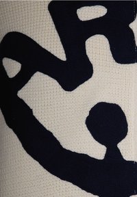 Maglione lavorato ai ferri con uno sfondo crema e grandi testi e forme blu navy. Il tessuto ha un aspetto morbido e texturizzato.