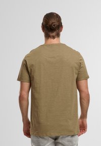 Olivgrön t-shirt med kort ärm och rund halsringning, tillverkad av mjukt material, med en enfärgad textur och en avslappnad passform.