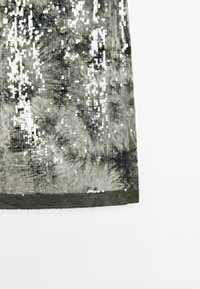 Jupe pailletée dans des nuances de gris avec une surface texturée. Présente un bord en forme de vagues et des reflets lumineux variés provenant des paillettes.