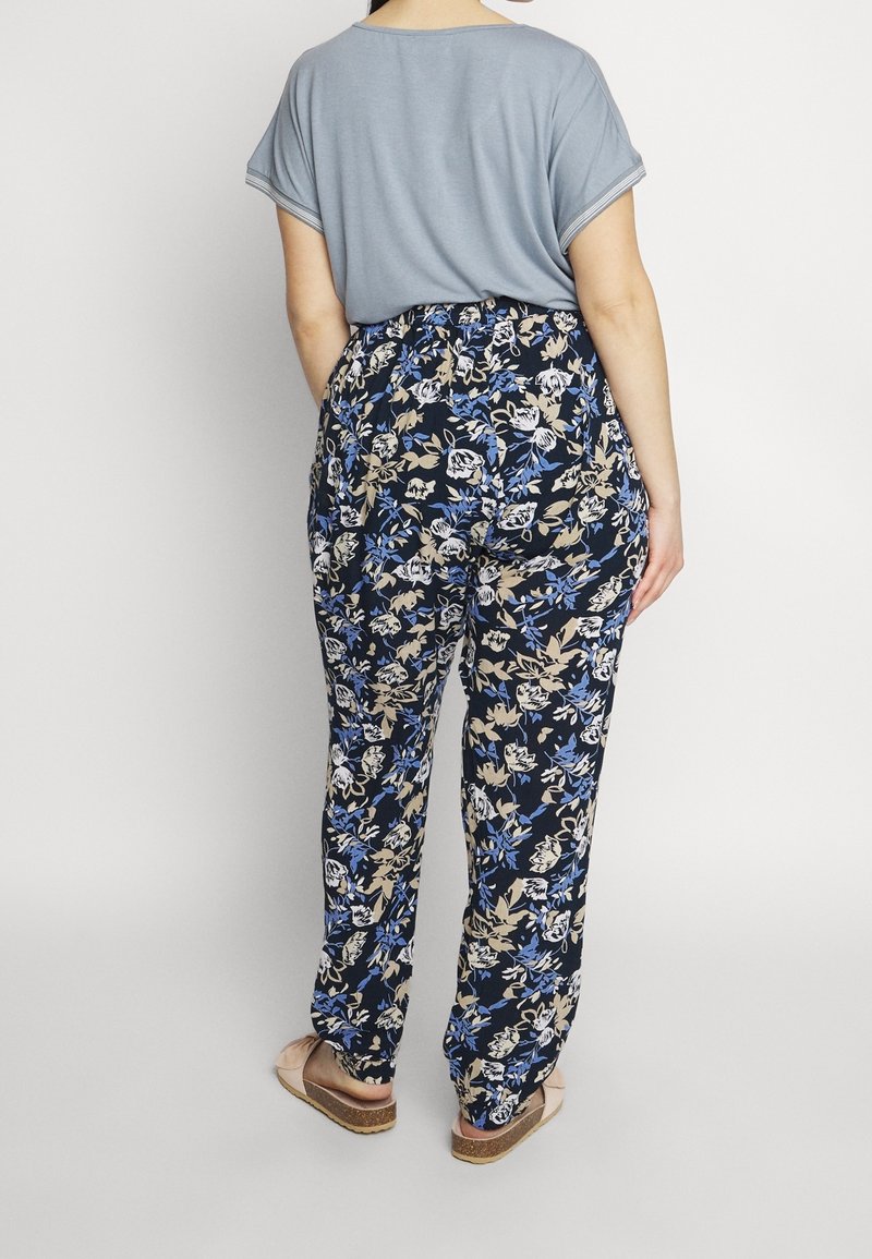 Haut bleu à manches courtes associé à un pantalon bleu marine à motifs floraux crème et bleus, coupe ample, et sandales plates couleur camel.