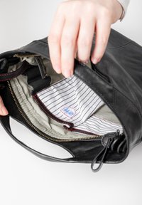 Sac en cuir noir avec une doublure en tissu rayé, des coutures rouges visibles et une fermeture éclair. En ouvrant le sac à la main, on découvre des poches intérieures.