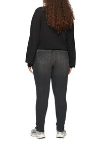 Zwart oversized sweater gecombineerd met donkergrijze skinny jeans. De jeans hebben een klassiek vijf-pocket ontwerp en zichtbare stiksels op de achterkant.