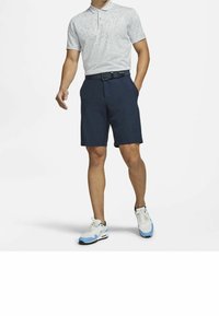 Mansoutfit med en ljusgrå polo med svarta prickar, blå shorts och vita sneakers med blå detaljer; bälte ingår.