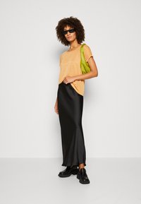 Svart sateng maxi skjørt, kortermet oransje topp, grønn bag, svarte plattformsko og svarte solbriller. Glatte teksturer, tettsittende design.