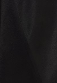 Svart tyg med en slät textur, som har en subtil glans och två överlappande sektioner som skapar ett diagonalt mönster.