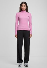 Helles rosa langärmliges Rollkragenoberteil mit schmaler Passform, kombiniert mit schwarzen weit geschnittenen Hosen; glatte Textur und Reißverschluss-Frontdetail.