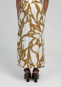 Jupe longue et fluide à base blanche arborant un motif abstrait marron audacieux. Taille élastique. Portée avec des sandales à talons marron.