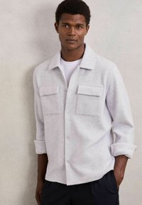 Heled hall button-up särk, mis on valmistatud pehmest kangast, kahel rinnataskul, rullitud varrukatega ja klassikalise kraedisegniga.