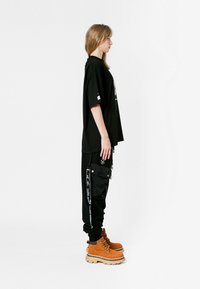 Camiseta negra de gran tamaño, pantalones cargo negros con bolsillos laterales, botas de estilo lace-up en color marrón claro con suela gruesa, silueta recta, diseño minimalista.