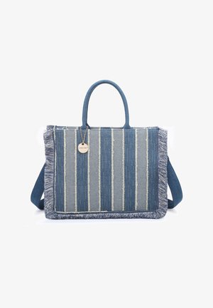 Blauwgrijs gestreepte stoffen shopper met franjes aan de randen, twee handvatten en een ronde metalen merkembleem die aan één handvat hangt.