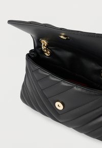 Čierna kožená prešívaná kabelka s prekladanou chlopňou, opatrená zlatým kovovým patentným zapínaním a detailom reťaze vo vnútri. Interiér je podšitý.
