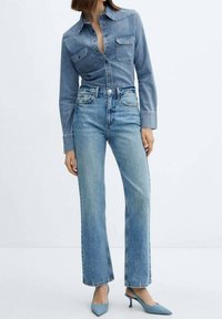 Chemise en denim avec deux poches poitrine, jean bleu taille haute à jambes droites, associé à des escarpins bleu clair à bouts pointus. Texture lisse, design décontracté.