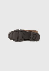 Brown suede sneaker with a thick black rubber sole featuring a textured surface and segmented tread pattern for grip.