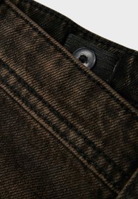 Close-up van donkerbruin denimstof met gedetailleerde stiksels en een zwarte knop die gedeeltelijk zichtbaar is op een tailleband.