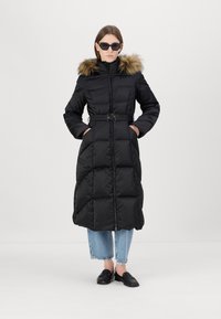 Juodas pūkinis paltas su kailiniu gobtuvu, diržu ant liemens ir užtrauktuku. Yra siuvinėtas dizainas, ilgos rankovės ir šoninės kišenės.