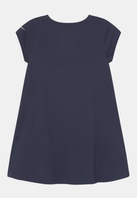 Námořnická modrá šaty s krátkým rukávem ve tvaru A s kulatým výstřihem a malým bílým zakřiveným detailem na levém rukávu.