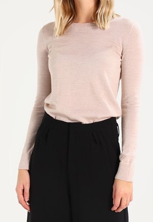 Woman wearing a light pink long-sleeve fitted shirt tucked into high-waisted black wide-leg pants with pleated details.