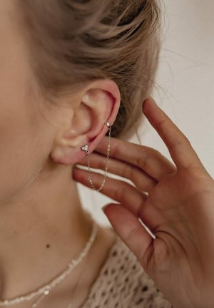 Silberne Kettenohrringe mit Herz Akzenten, bestehend aus einer feinen Kette, die zwei Stecker verbindet, getragen am linken Ohr, schlichtes Design, eleganter Abschluss.