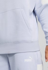 Lichtblauwe trui met een voorzak, geribbelde manchetten en een bijpassende tailleband. Beschikt over een wit Puma-logo aan de onderkant aan de rechterkant.