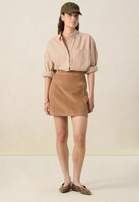Brown corduroy mini skirt with front pockets, paired with a beige and white striped button-up shirt and a leopard print cap.