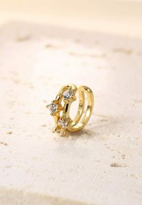 Goldring mit drei klaren Edelsteinen, einem einzigartigen Design aus verschlungenen Formen und polierter Oberfläche, vor einem neutralen Hintergrund.