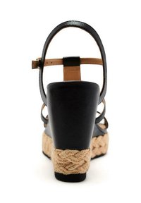 Sandalia de cuña de cuero negro con correa de tobillo en tono marrón y plataforma de yute trenzado. Presenta un diseño de punta cerrada y un tacón curvado para mayor soporte.