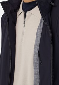 Mans zip-up jacka med ett svart ytterskikt, en beige texturerad innerskikt och grå detaljer. Inkluderar en sidodragkedjeficka.