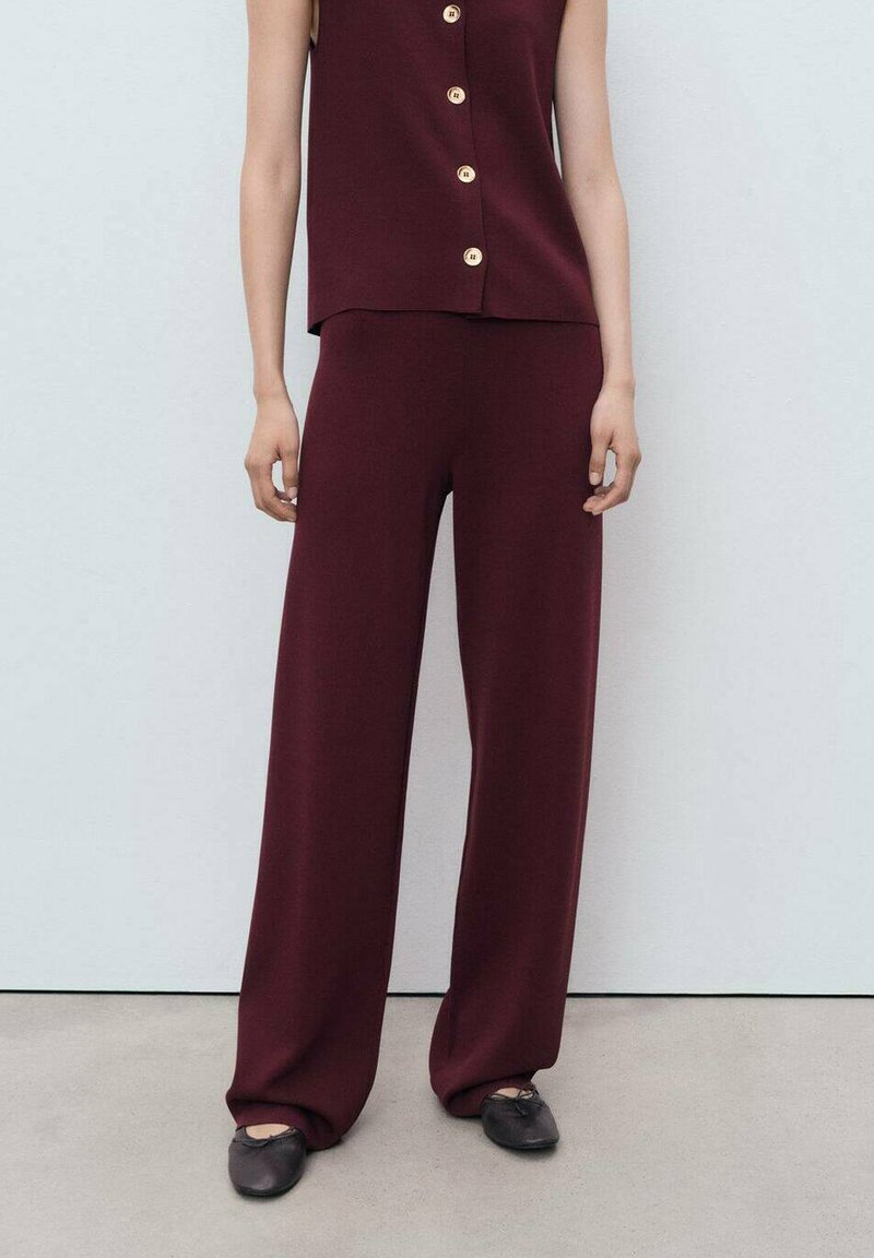 Bordeaux mouwloze top met knopen aan de voorkant, gecombineerd met wijde broek in dezelfde stof. Glad oppervlak, minimalistisch ontwerp en relaxte pasvorm.