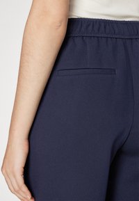 Pantalones azul marino con una textura suave, que cuentan con una cinturilla elástica y un pequeño bolsillo trasero. La tela parece ligera y cómoda.