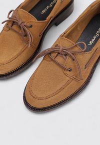 Braune Wildlederschuhe mit glatter Textur, runder Zehenform und Lederbändern. Sie haben eine kontrastierende braune Sohle mit erhöhten Kanten.