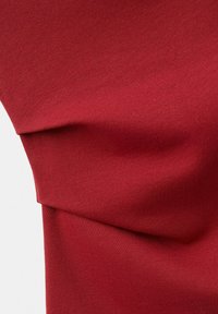 Tissu rouge lisse plié avec une texture visible et des ombres douces sur un fond clair.