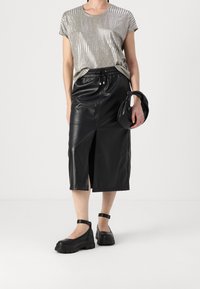 Stříbrný metalický top s krátkým rukávem, černá kožená midi sukně se štěrbinkou v přední části a chunky černé platformové boty s kotníkovými pásky.