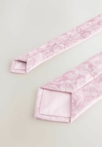 Világos rózsaszín nyakkendő virágmintával, texturált anyagból készült. A végek ferdén vágottak, sima belsővel és látható varrási részletekkel.