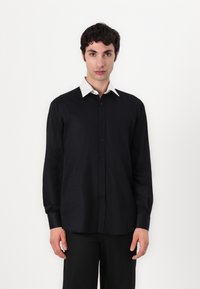 Svart langermet skjorte med en kontrastfylt hvit krage, knapp-ned design, og lett tekstur. Har en avslappet passform og minimalistisk stil.