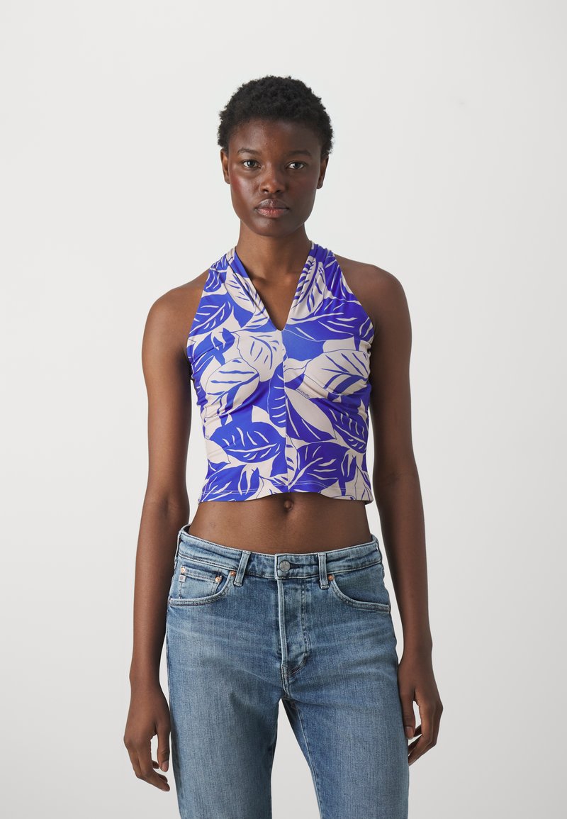Crop top i blå og lys beige, med et bladmønster. Materialet virker glatt med V-halsdesign, parret med lyse denimjeans.