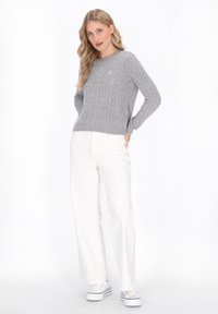 Grauer Kabelstrickpullover mit langen Ärmeln und rundem Ausschnitt; kombiniert mit weißen, weit geschnittenen Hosen und weißen Sneakers mit schwarzen Streifen.