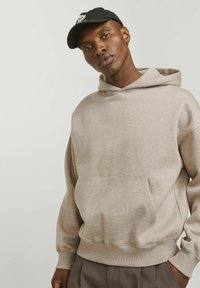 Beige hoodie made of soft fabric with a front pocket, adjustable hood, and ribbed cuffs. A subtle logo is stitched on the chest.